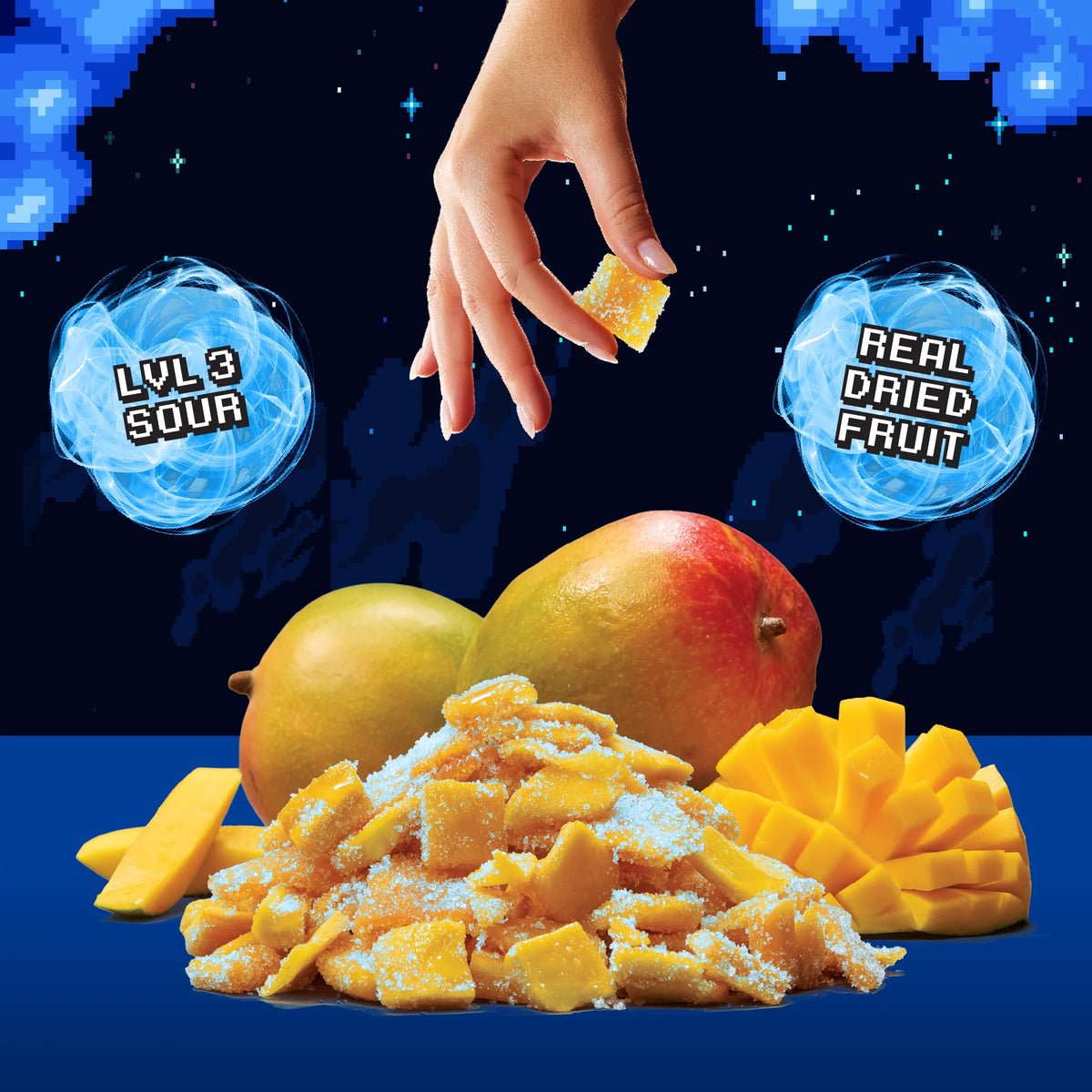 A pile of sugar-coated dried mango pieces with whole and sliced mangoes beside them, set against a dark starry background. A human hand is reaching in from the top to grab a piece of mango, with two blue circular callouts reading 'LVL 3 SOUR' and 'REAL DRIED FRUIT'.